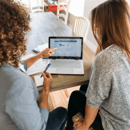 Echanges entre collaboratrices, assises à un bureau et montrant l'écran d'un ordinateur portable.