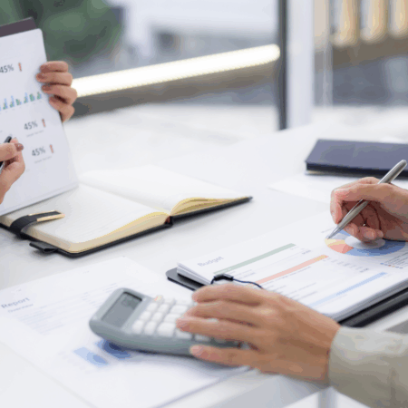 Gros plan sur deux mains et des documents, notamment une calculatrice et un agenda.